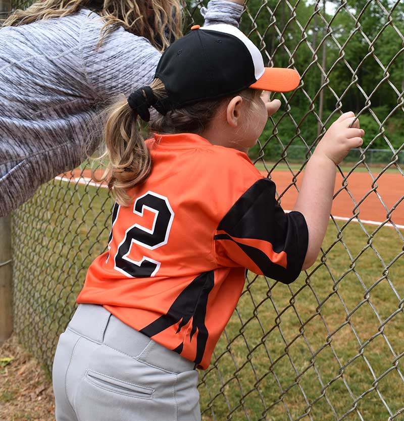 Tucker youth baseball player peers through fence. 