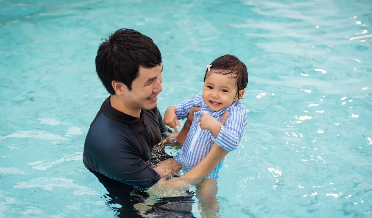 Dad holding toddler daughter in a pool.